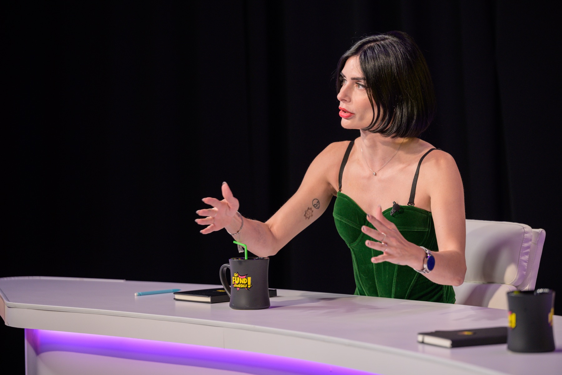 Carina in green velvet, speaking as a guest Titan on Go Fund Yourself!
