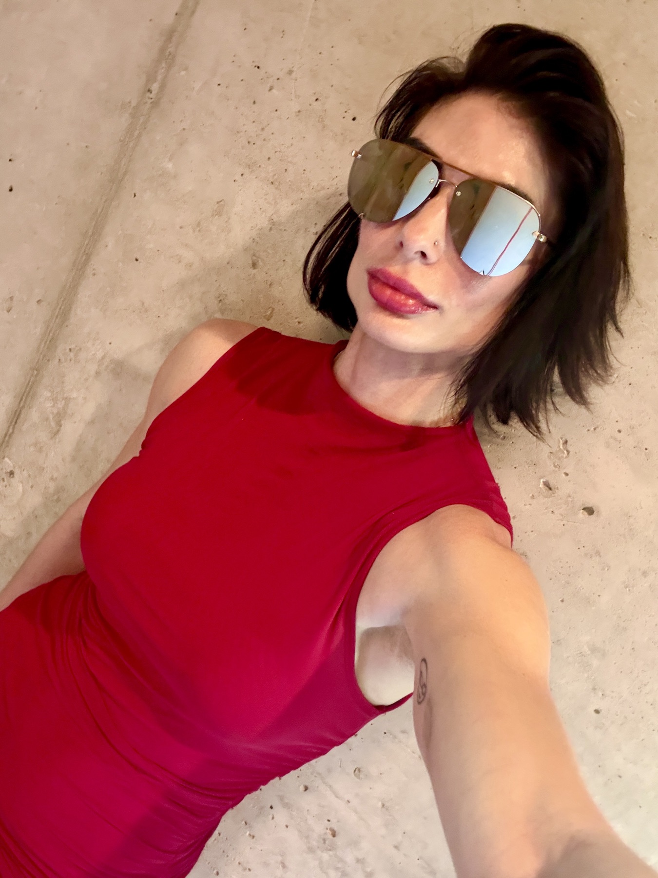 Carina in a red dress and mirrored aviators, lying on concrete
