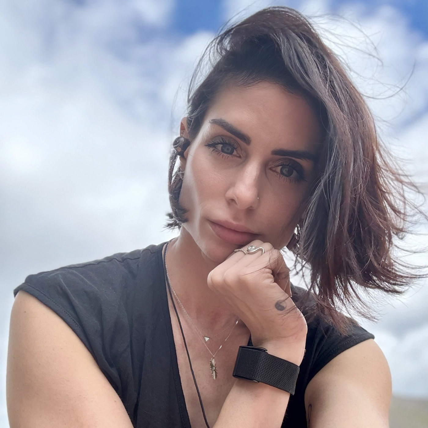 Carina in thought, hand at her chin, against a cloudy sky